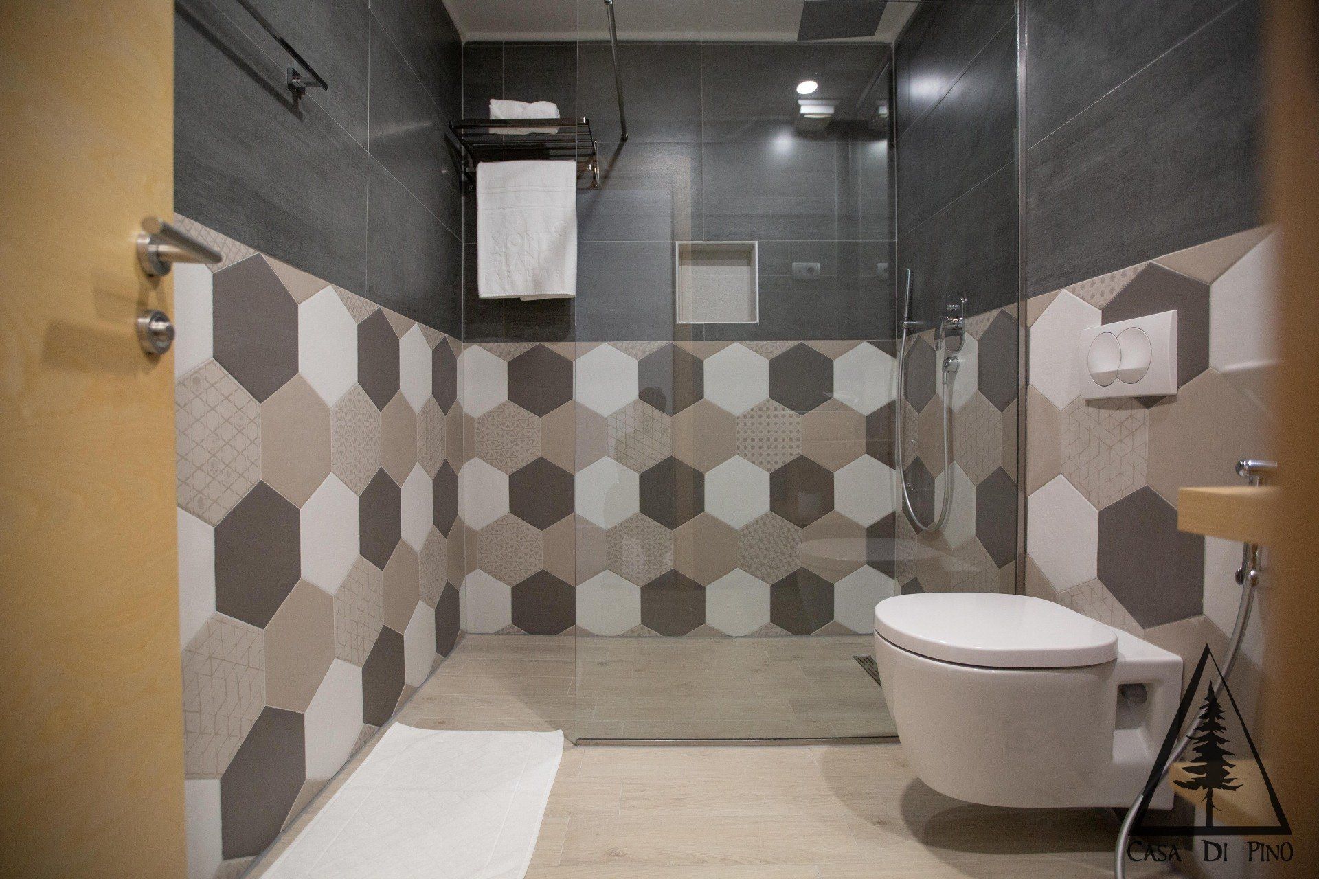 A bathroom with black, grey and white tiles, a toilet, sink and shower.