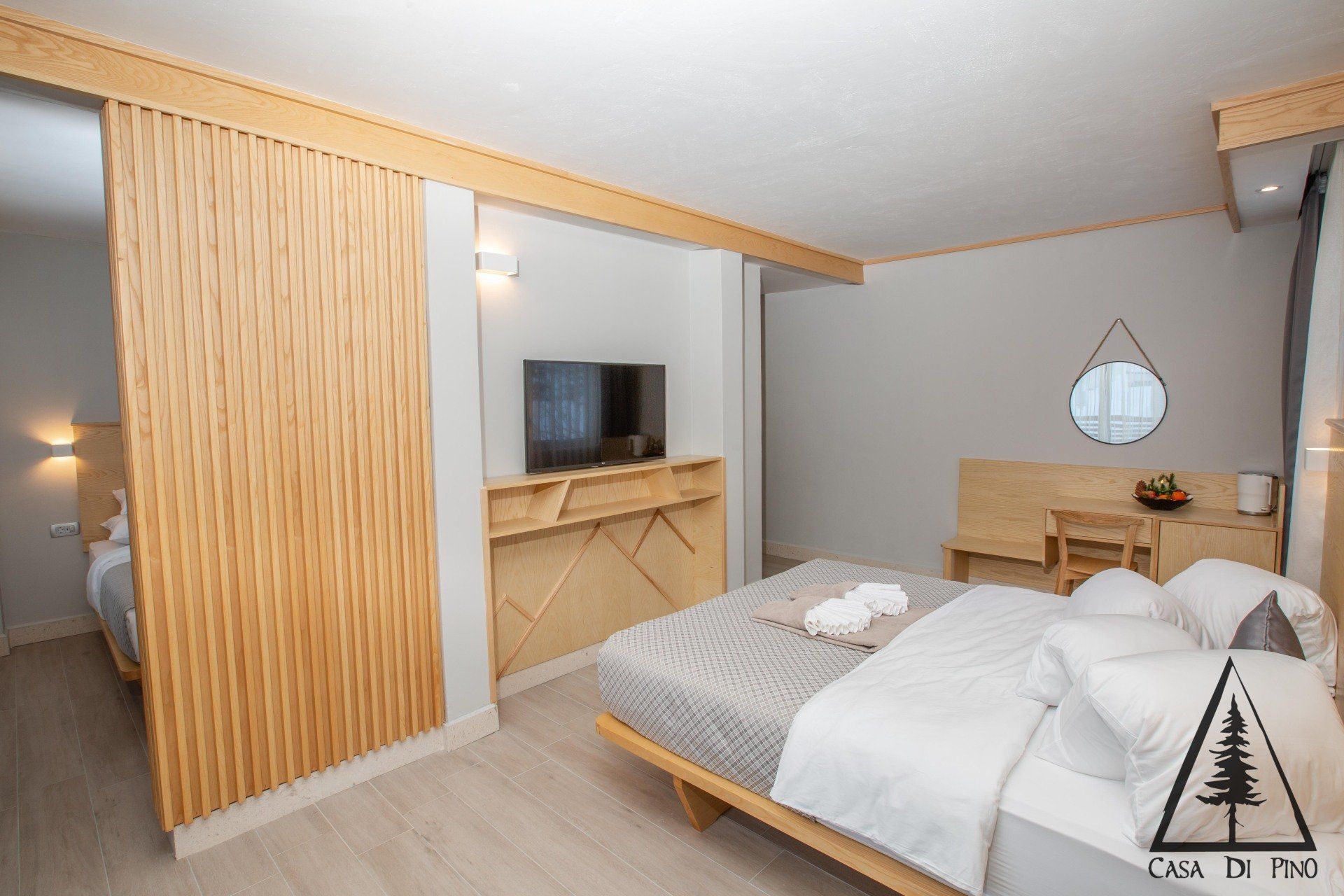 A hotel room with a king size bed, flat screen TV, wooden details on the wall, desk and mirror.