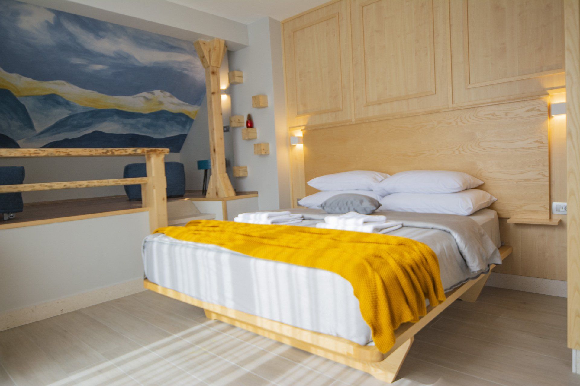 A hotel room with a king size bed and a blue and yellow mural on the wall and a small galery.