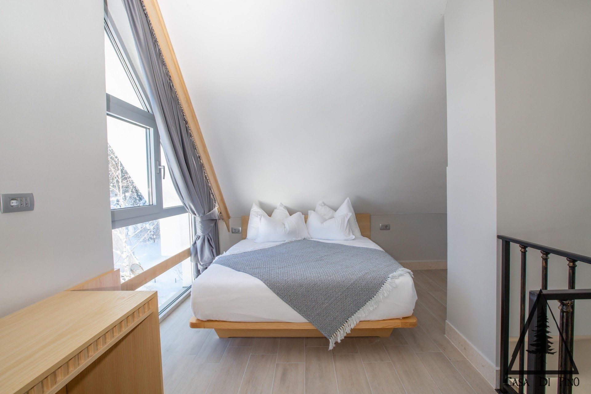 A bedroom with a bed , stairs and a large window.