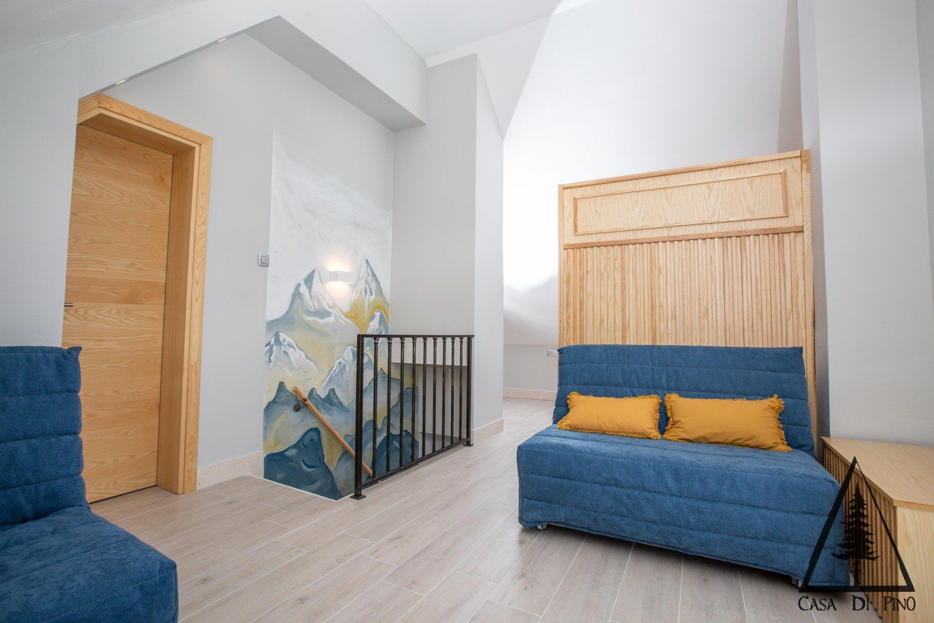 A bedroom in a penthouse with a blue couch and yellow pillows and a big light wall mural.