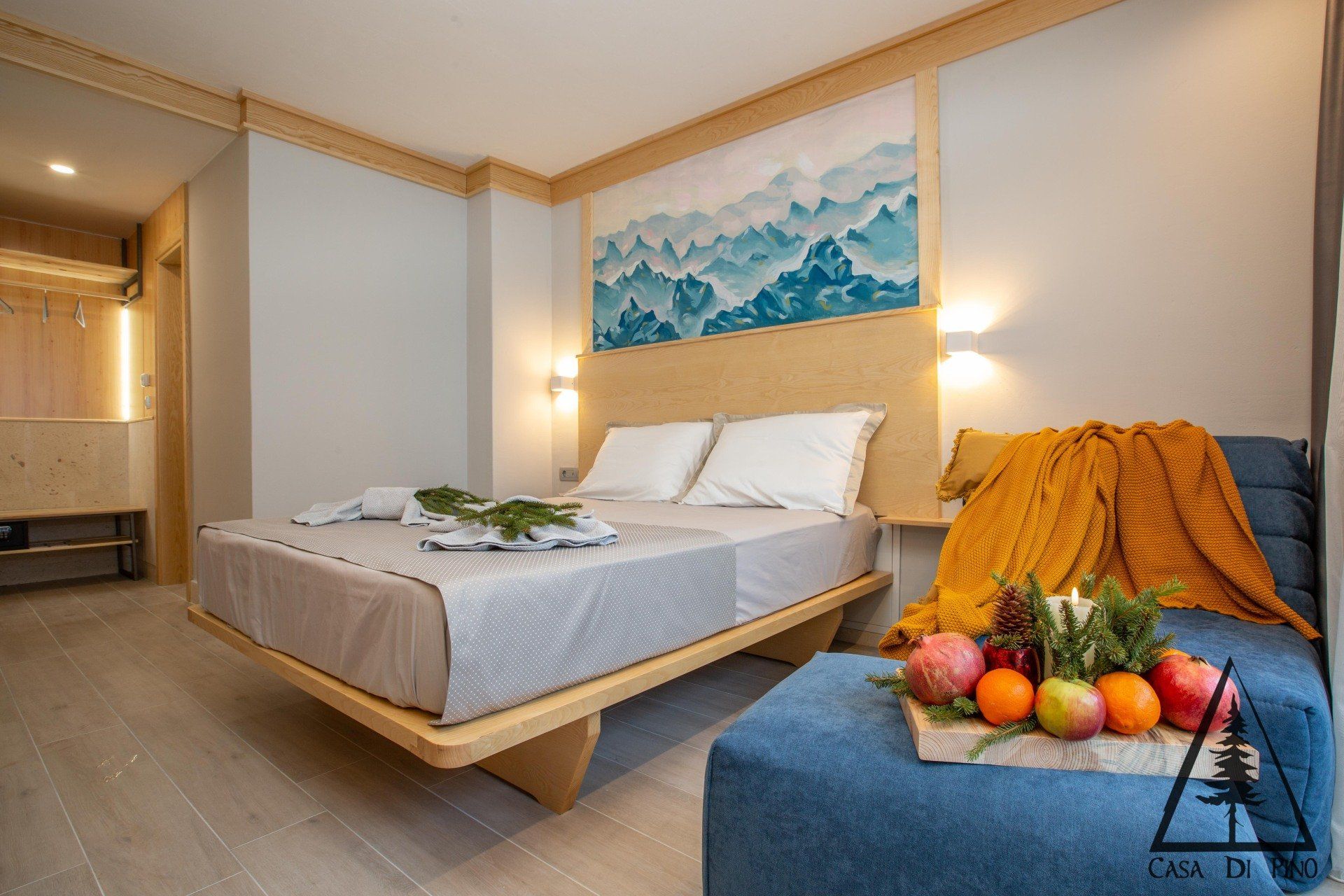A hotel room with a bed, wall mural over the bed, couch, and fruit on the side table.