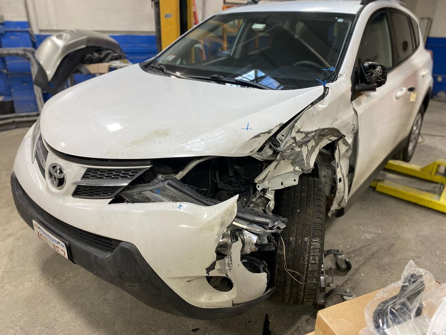 White Toyota SUV with significant front-end damage, likely from a collision, in a repair shop.