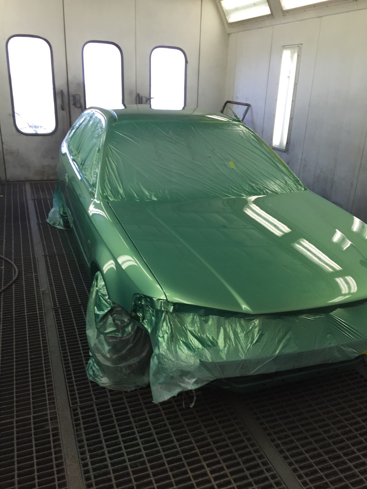Green car in a paint booth, covered in plastic wrap.