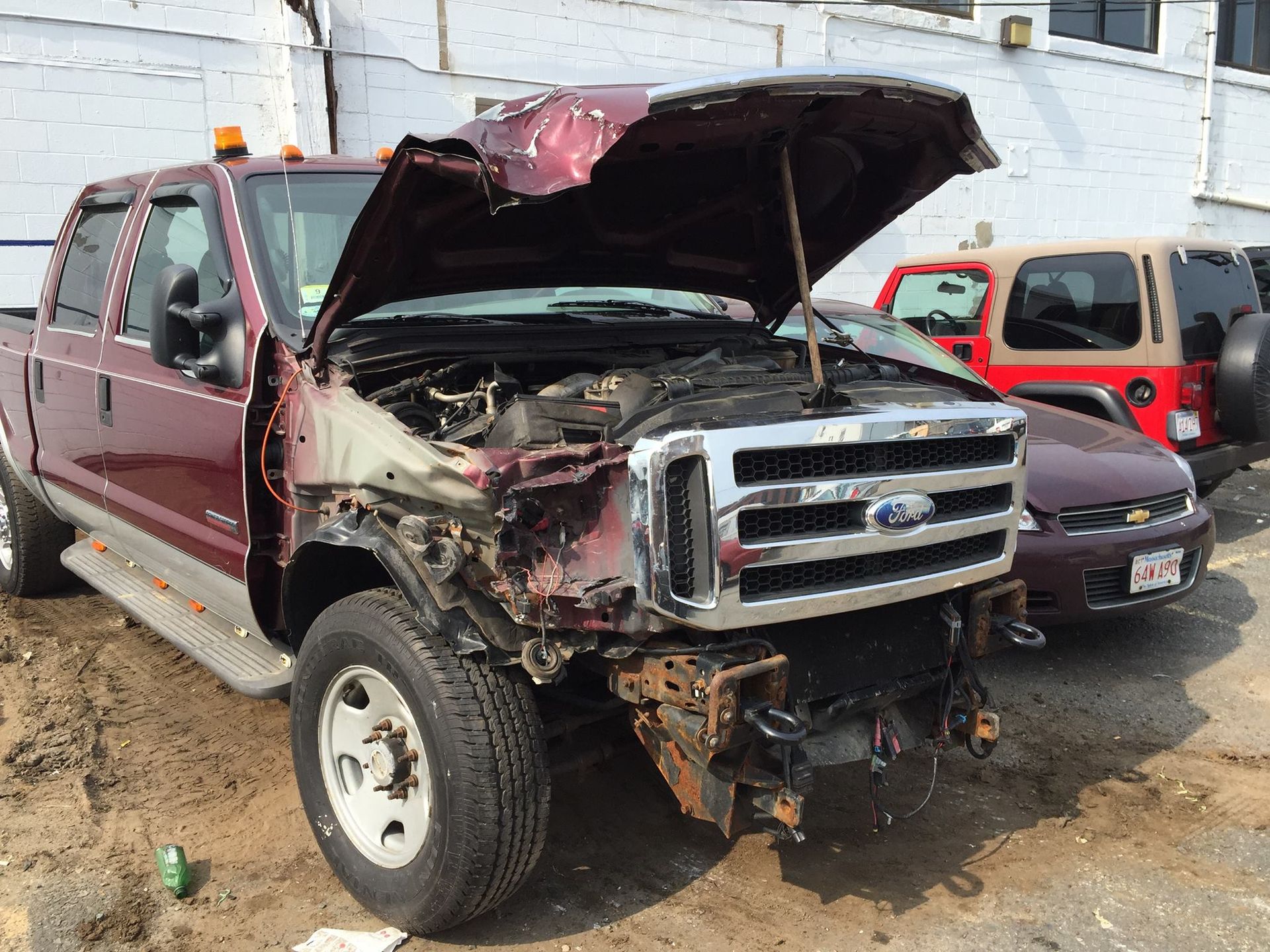Damaged maroon Ford pickup truck with open hood, showing extensive front-end damage.