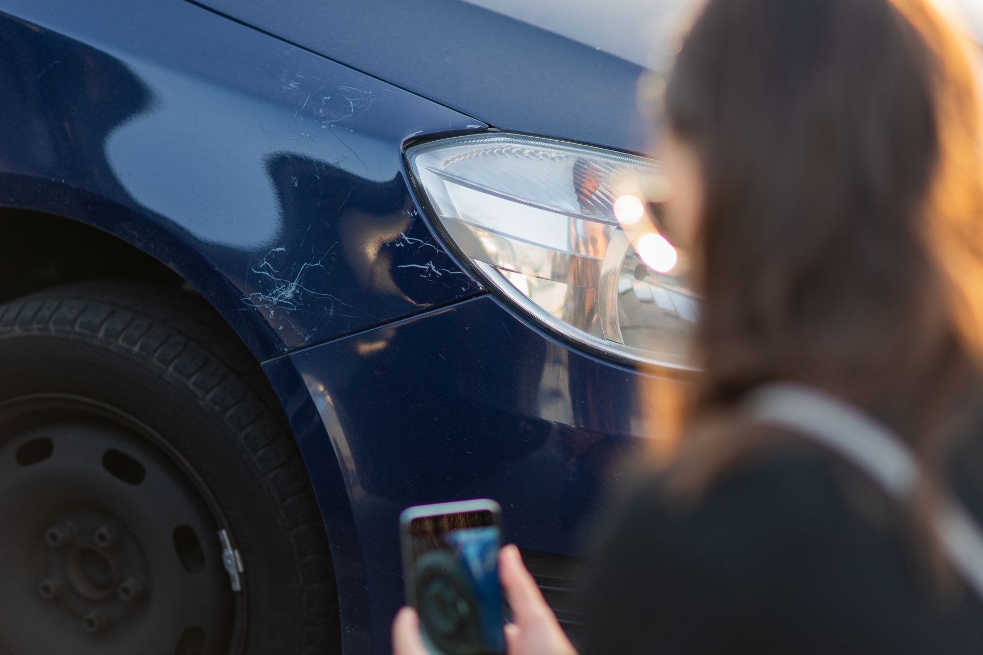 Person taking photo of damaged blue car fender with a smartphone. Person taking photo of damaged blue car fender with a smartphone.