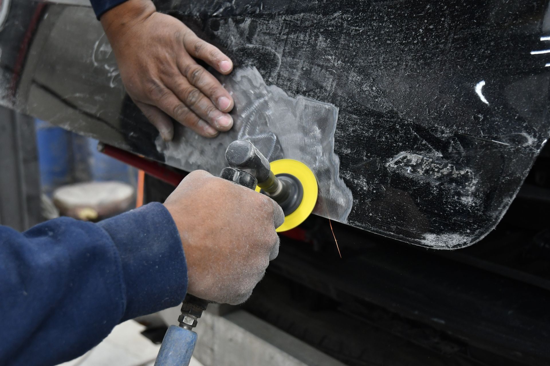 Person sanding a car panel with a power sander; body shop.