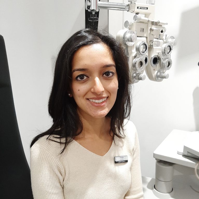 Woman smiling in an eye exam room beside an optometry machine
