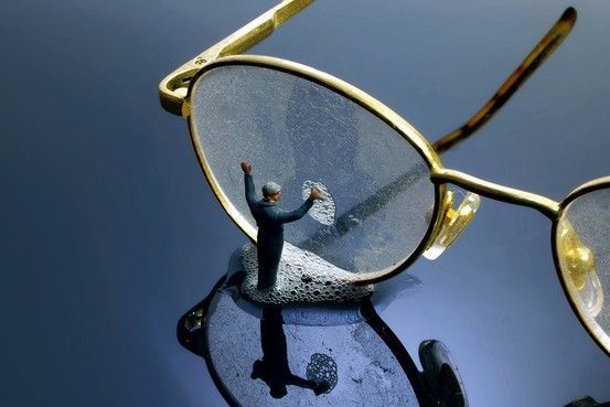 Gold eyeglasses with a tiny figurine reflected in one lens on a blue surface