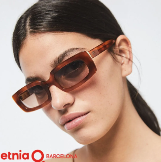 Woman wearing brown rectangular sunglasses with the etnia Barcelona logo on a white background