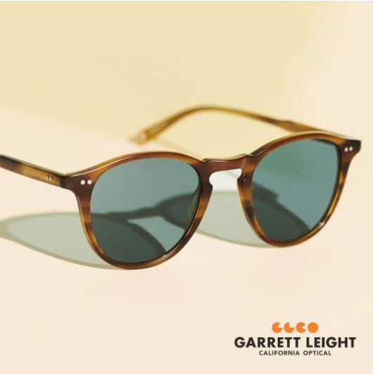 Brown sunglasses with blue-green lenses on a beige background, Garrett Leight logo at bottom right