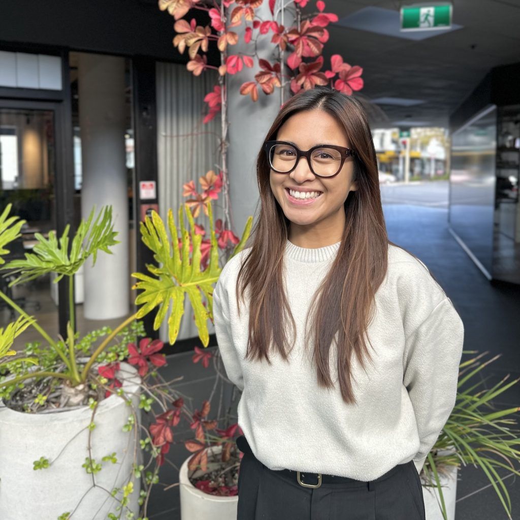 Smiling person in glasses standing by potted plants in an indoor walkway