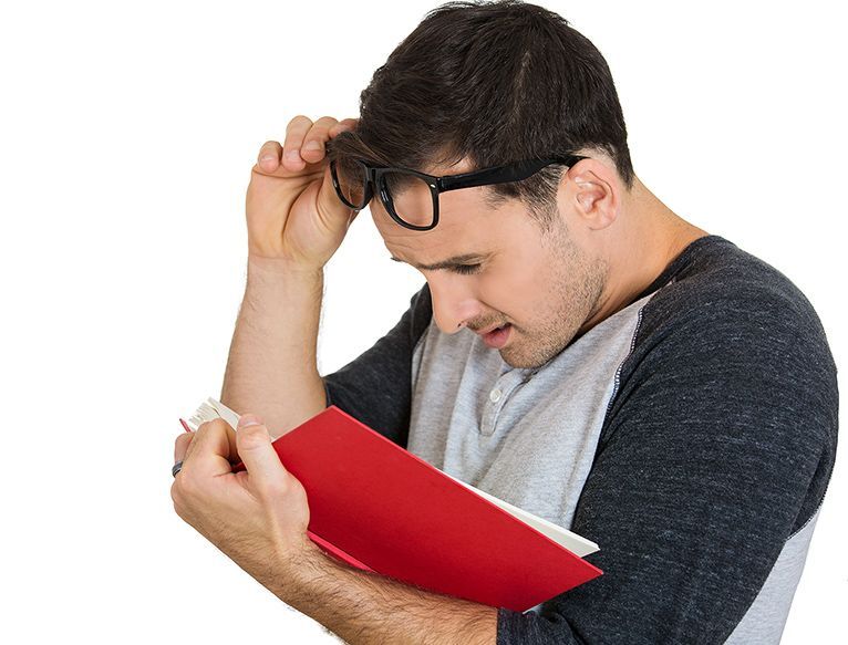 Man studying a red notebook, holding his glasses with a focused expression