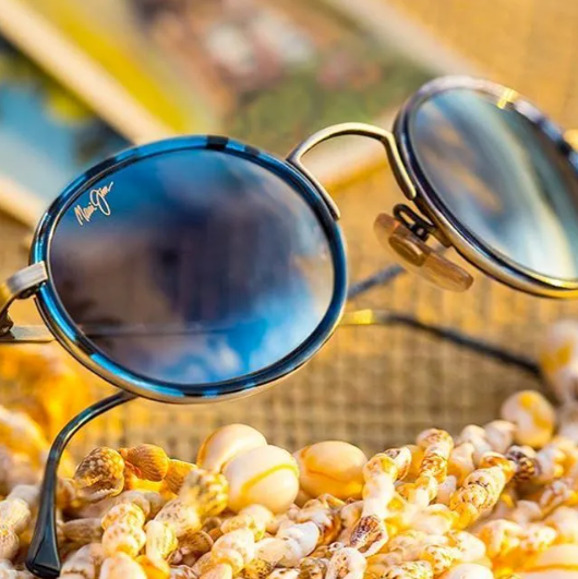 Blue round sunglasses resting on seashells with a blurred beach background