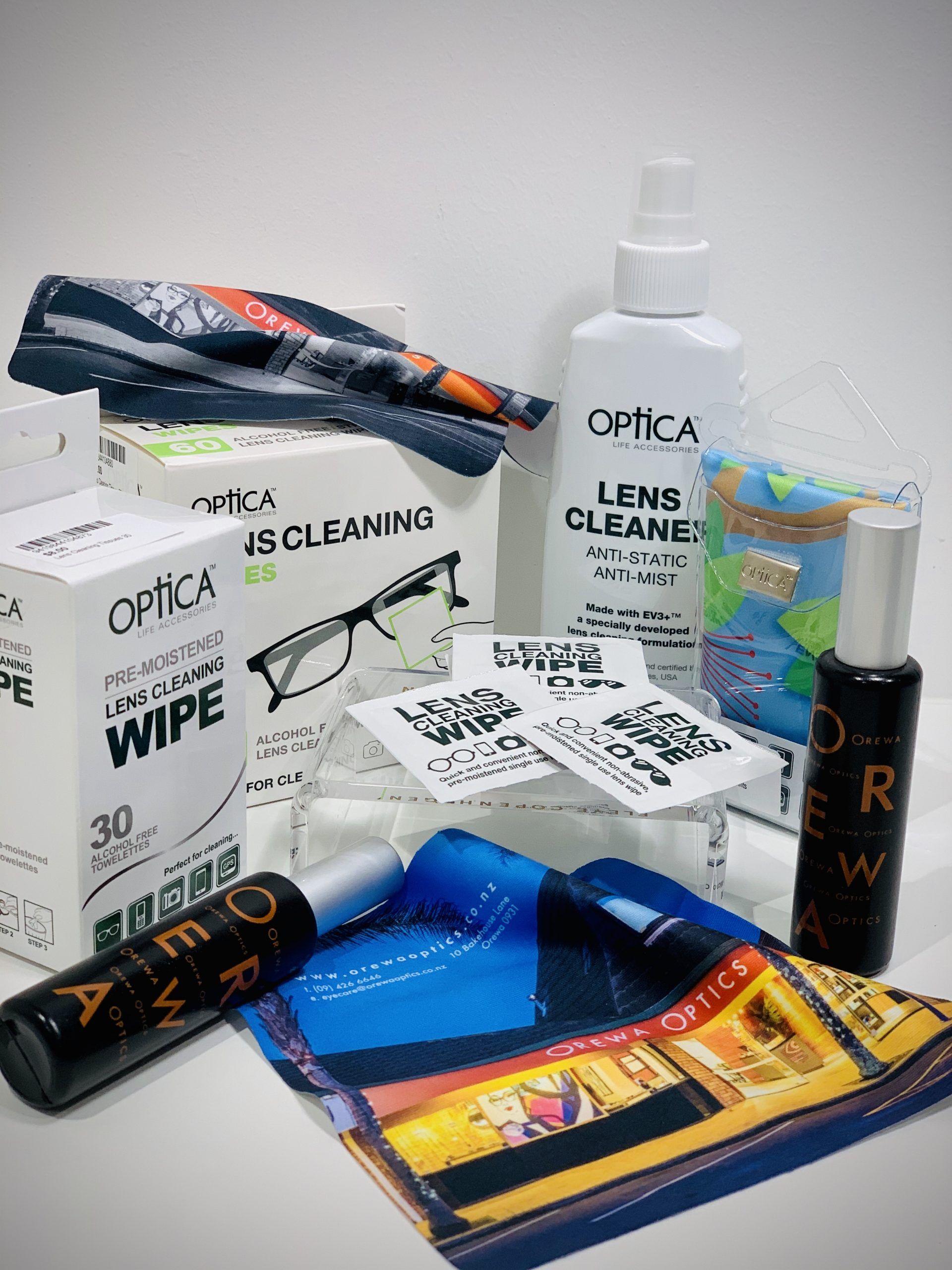 Assorted OptiCa lens-cleaning products and wipes arranged on a white surface.