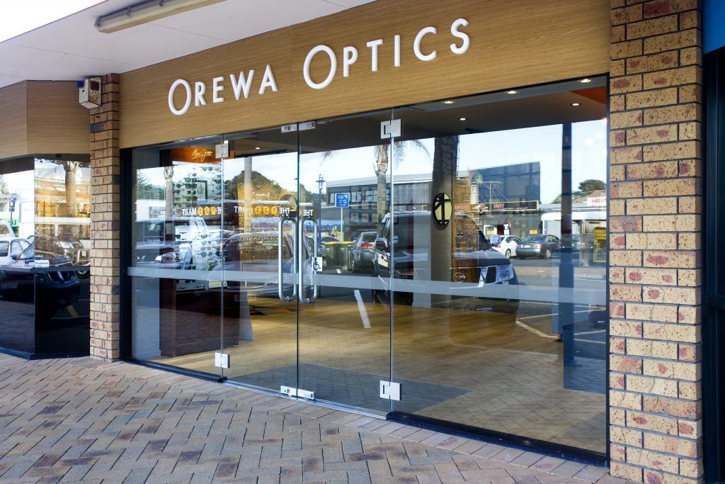 Storefront of Orewa Optics with large glass windows and brick exterior under a covered walkway