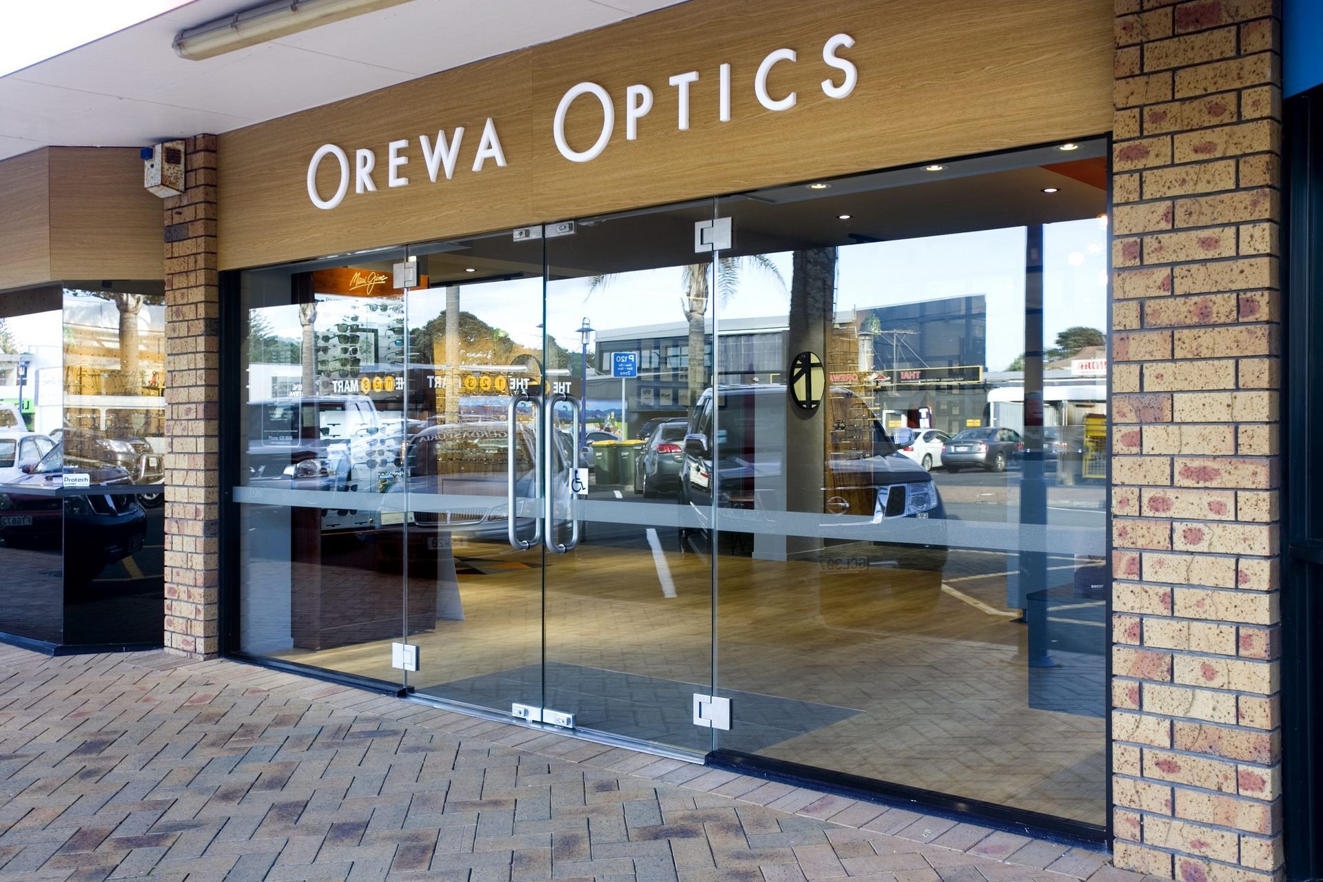 Storefront of Orewa Optics with large glass windows and brick exterior in a shopping center