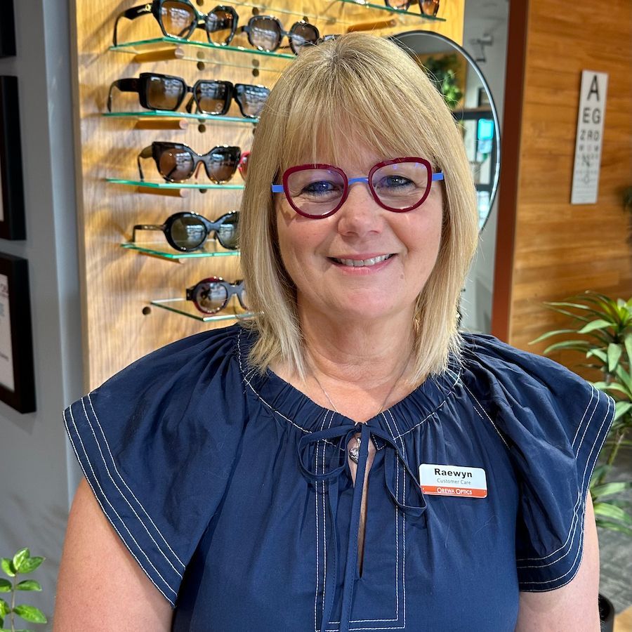 Smiling woman in glasses and navy blouse standing in an eyeglass store display area