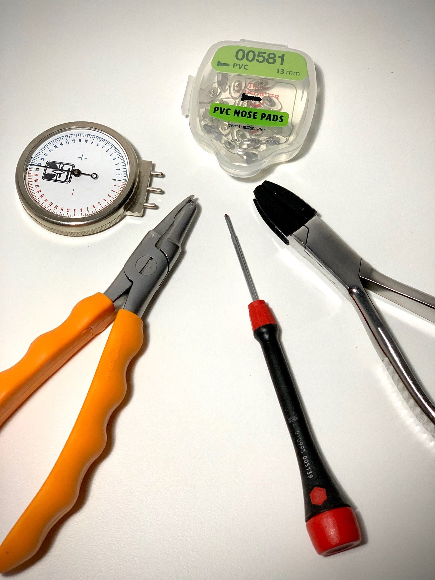 Several tools on a white background: pliers, a screwdriver, a utility knife, a tape measure, and a small gauge.