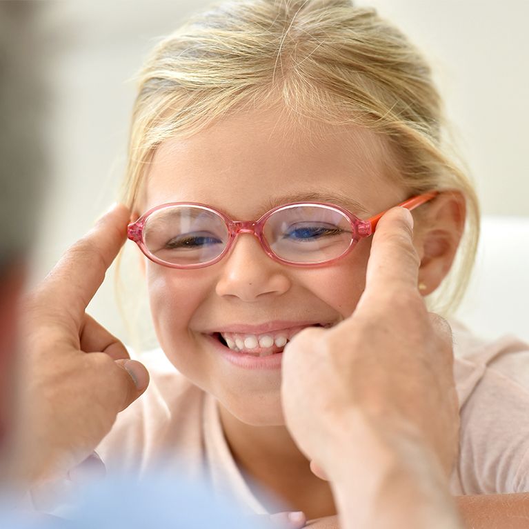Child smiling as red glasses are adjusted by adult hands
