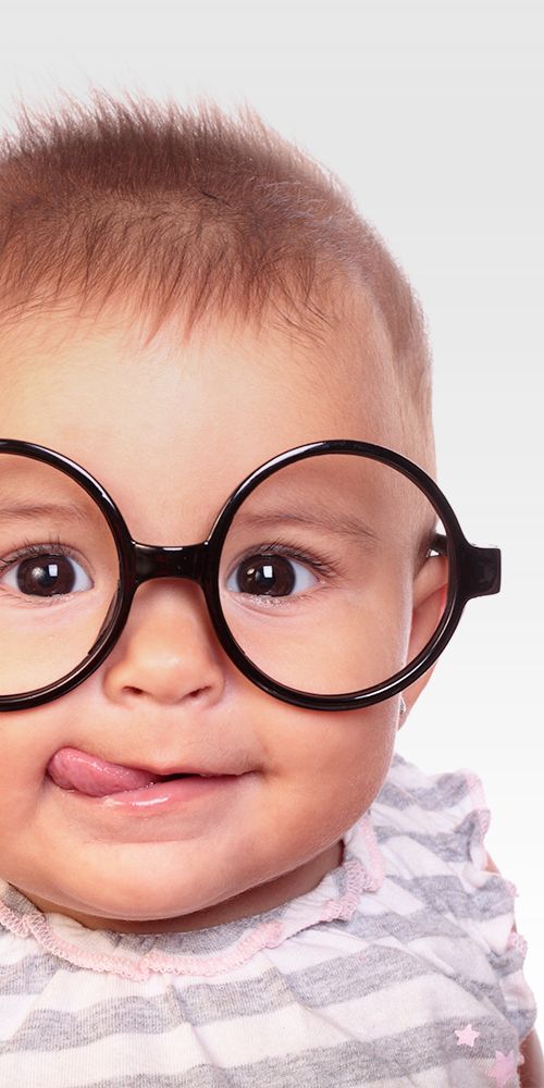 Baby wearing oversized round black glasses, smiling against a light background