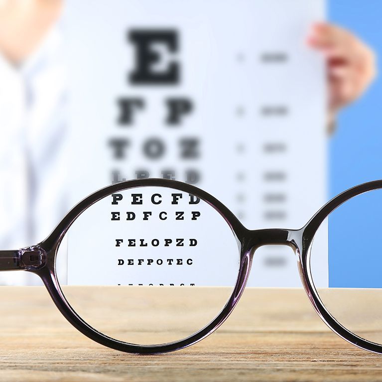 Eyeglasses magnifying an eye chart on a table, with a blurred eye test chart in the background