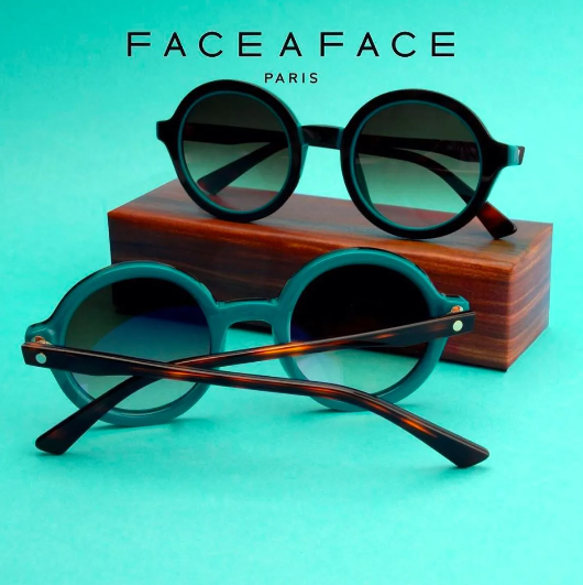 Two pairs of round sunglasses on a wooden block against a turquoise background, with Face a Face Paris text