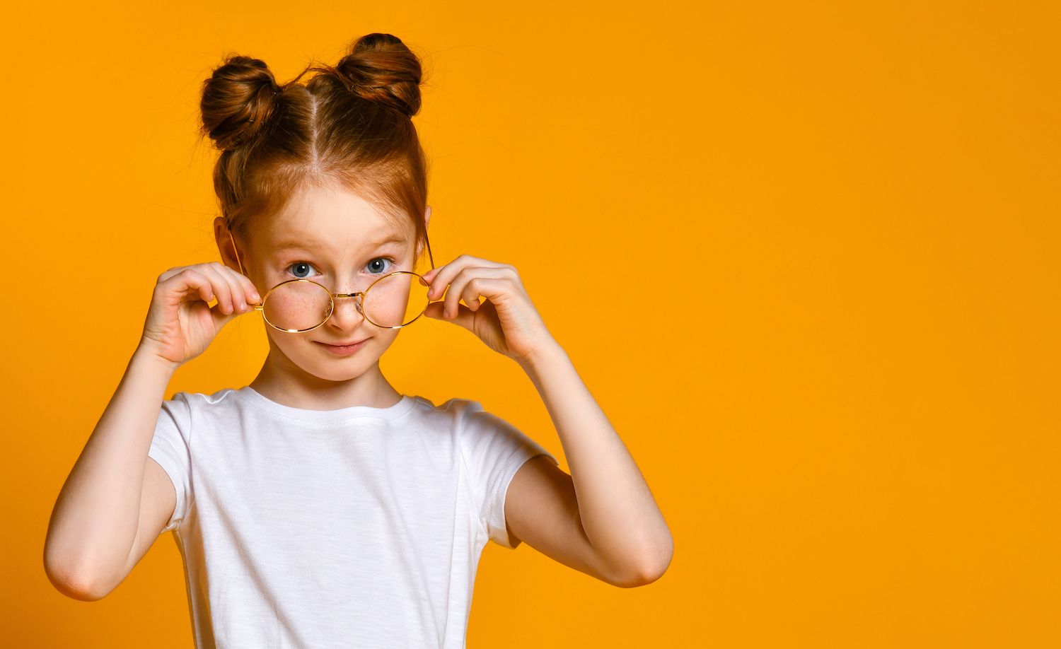 Child holding orange glasses and smiling against a bright orange background