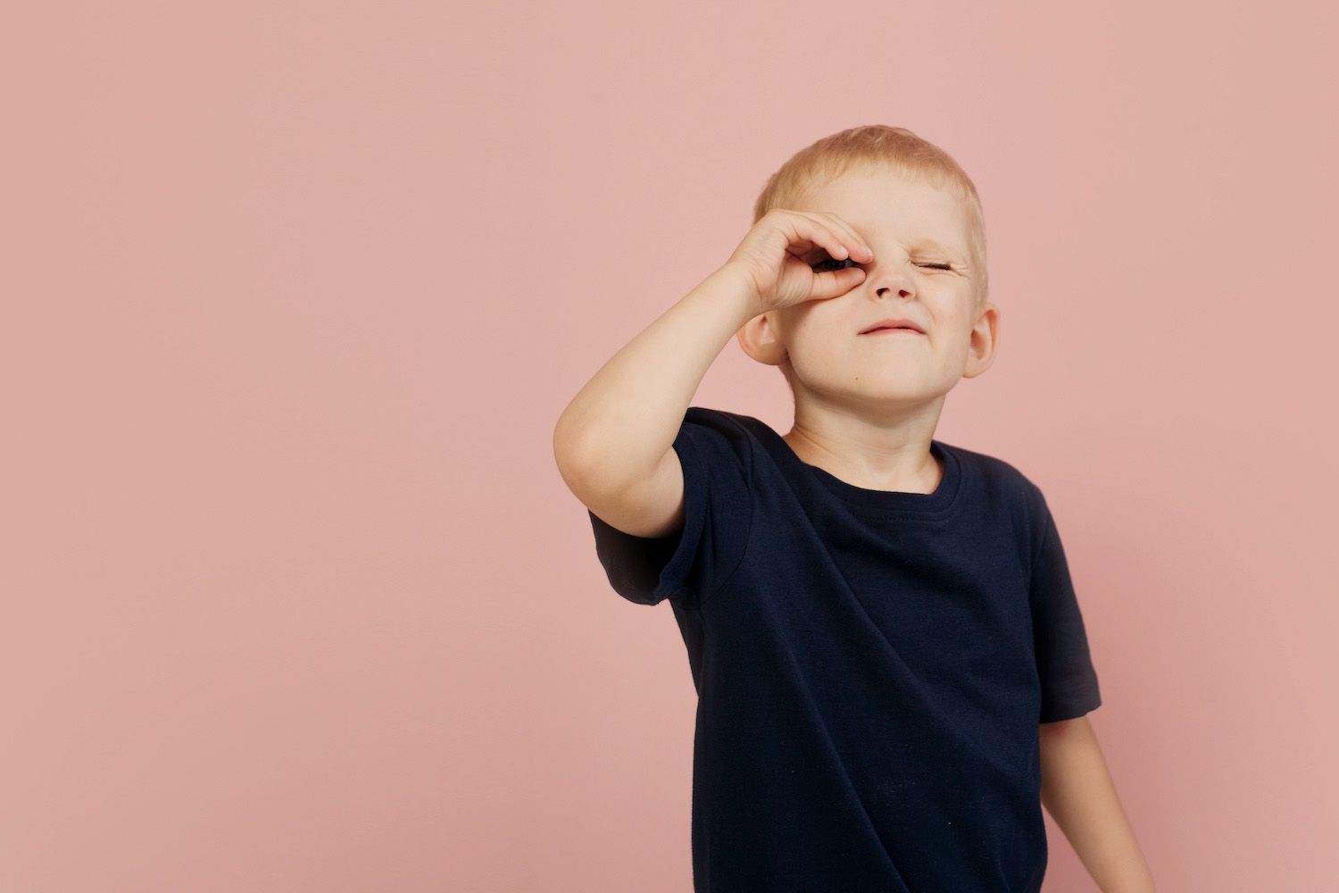 Boy in a dark shirt making a playful hand gesture against a pink background