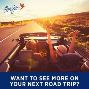 Convertible driving down a sunlit road with two people raising their arms, at sunset