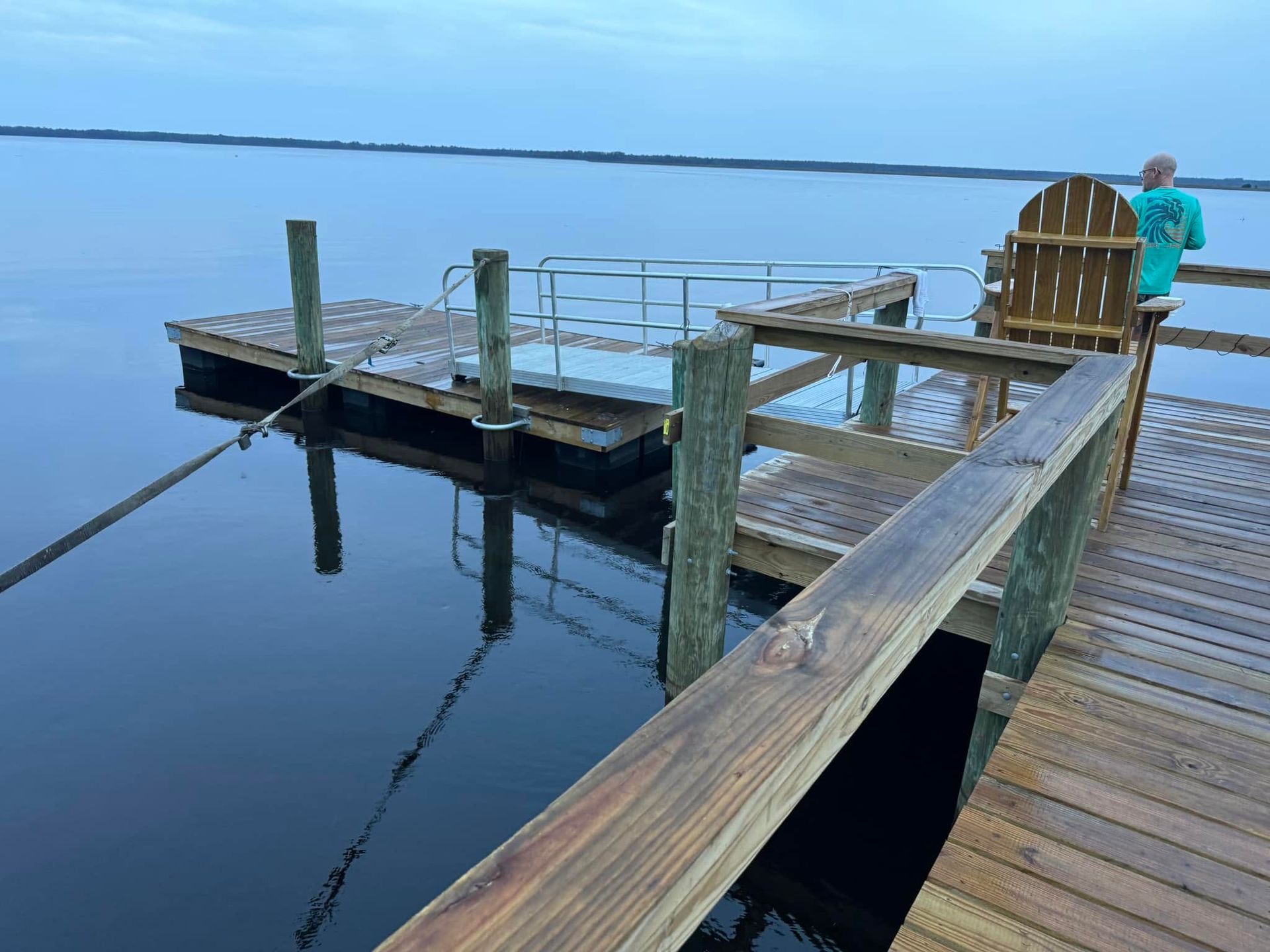 Wooden dock extending into calm blue water, with a person standing near the end.