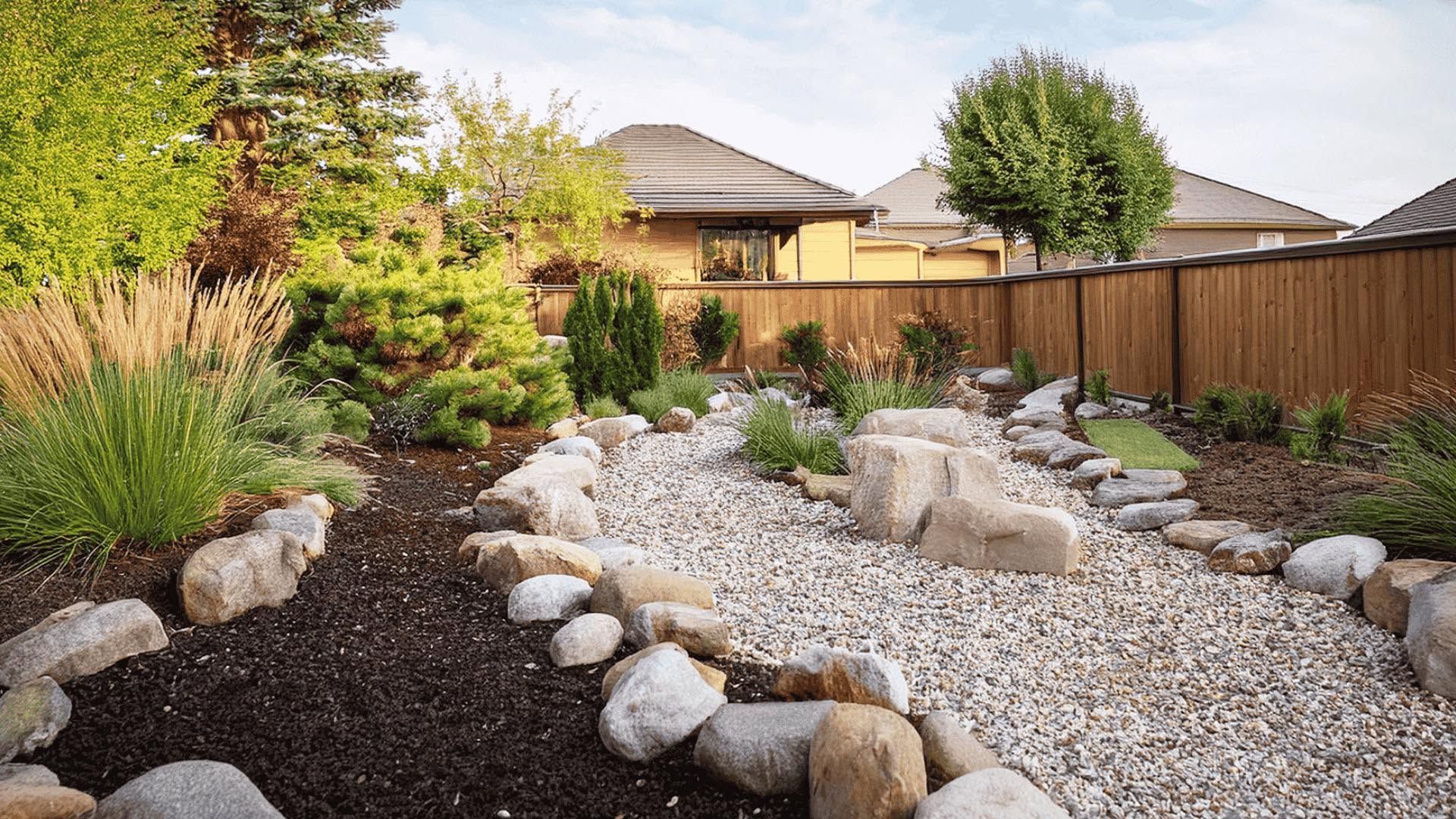Rock garden with white gravel, large stones, shrubs, and a wooden fence in a suburban backyard