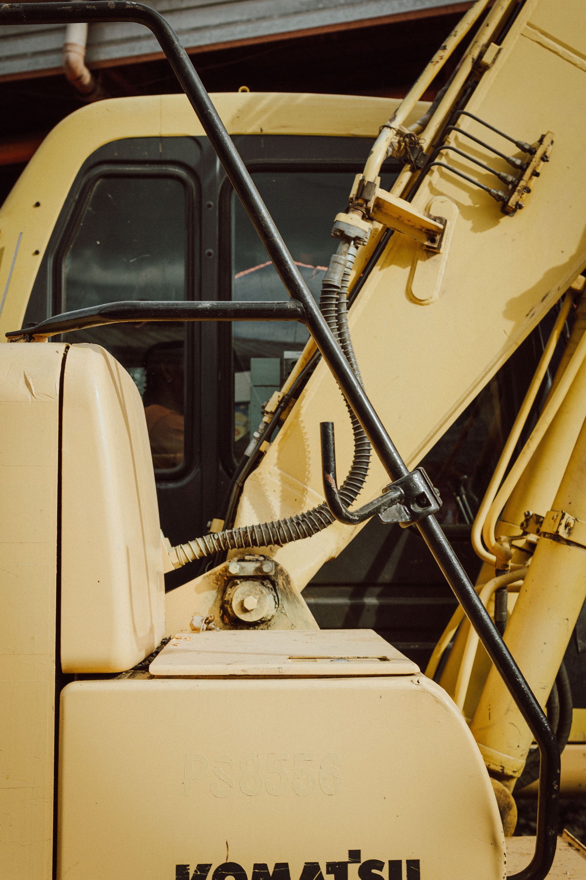 Yellow construction vehicle cab and hydraulic arm with black hoses and metal framework