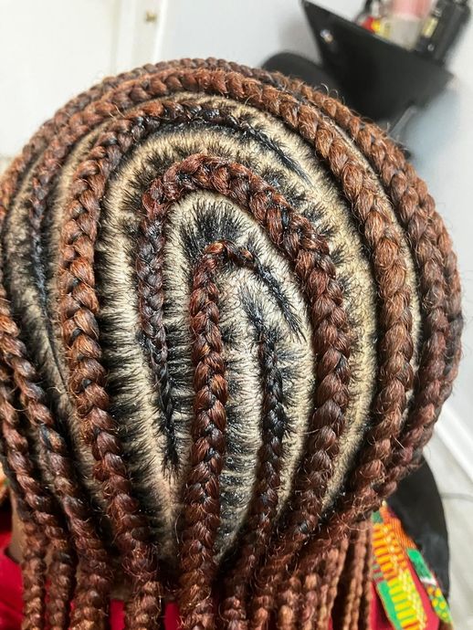 A top view of dark hair styled in intricate, curved cornrows with reddish-brown braiding hair extensions.