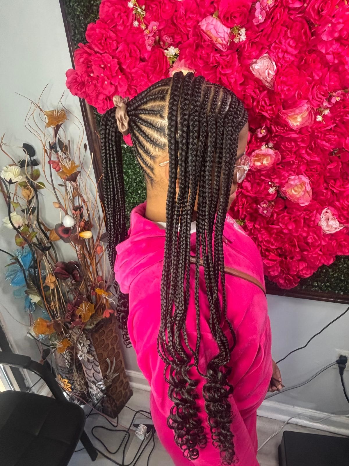A side view of a person with long, dark, braided hair styled into two high ponytails with curly ends, wearing a pink hoodie.