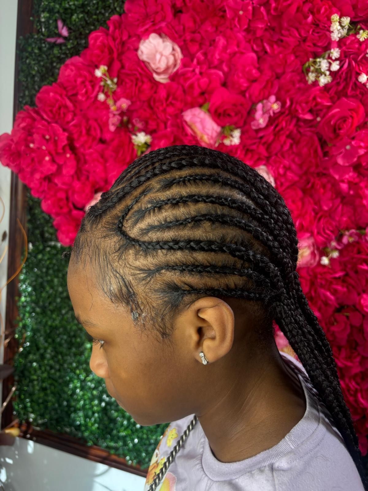 A person with neatly braided hair worn in cornrows against a bright, textured floral background.