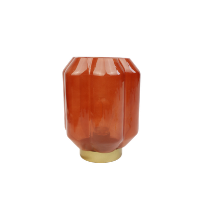 Een lampje van terracotta-kleurig glas met verticale ribbels, geplaatst op een metallic gouden voet.