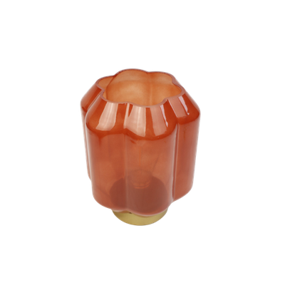 Een lampje van terracotta-kleurig glas met verticale ribbels, geplaatst op een metallic gouden voet.