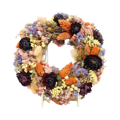 Een kleurrijke, ronde krans gemaakt van gedroogde bloemen en planten in paarse, oranje, roze en gele tinten.