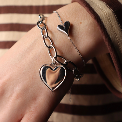 Een zilverkleurige schakelarmband met een grote, hartvormige hanger met een gepolijst, reflecterend middenstuk.