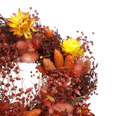 Een krans van gedroogde bloemen met warmgele bloemen, oranje pluimen en roodachtig blad op een witte achtergrond.