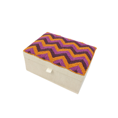 Een rechthoekig sieradendoosje met een beige stoffen omhulsel en een deksel met een levendig paars en oranje chevronpatroon.