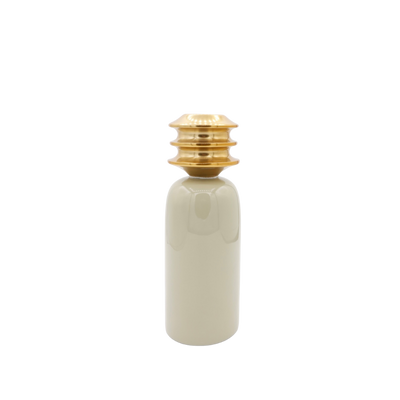 Een cilindervormig, beige keramisch object met een opvallende, gelaagde, goudkleurige metallic dop op een witte achtergrond.