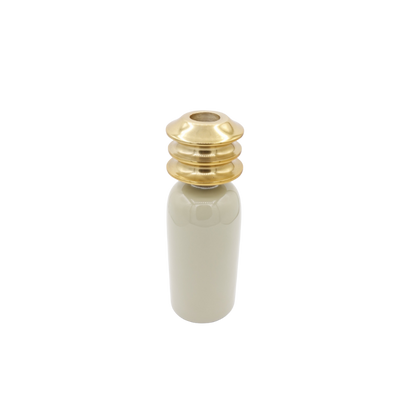 Een cilindervormig, beige keramisch object met een opvallende, gelaagde, goudkleurige metallic dop op een witte achtergrond.