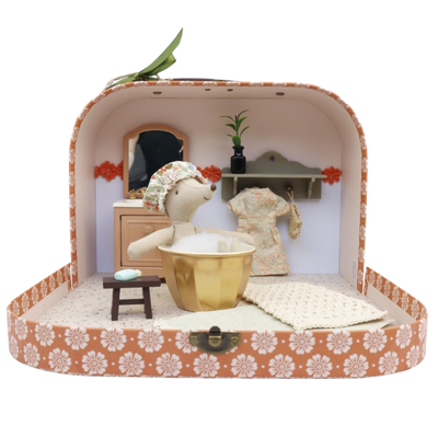Een klein stoffen muisje zit in een gouden badje in een versierde koffer die is omgebouwd tot een miniatuurbadkamer.