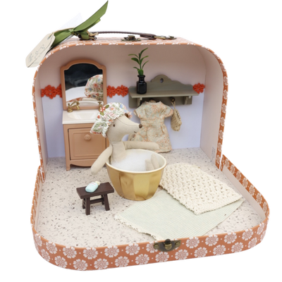 Een klein stoffen muisje zit in een gouden badje in een versierde koffer die is omgebouwd tot een miniatuurbadkamer.