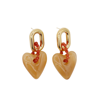 Ovale oorringen in goudkleur met een koortje van rood-oranje kralen dat verbonden is met een glad perzikkleurig hartje.
