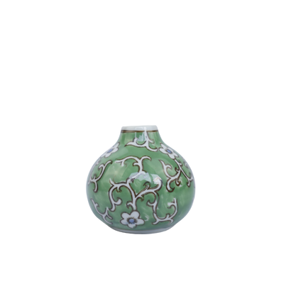 Een kleine, ronde, groene keramische vaas met een wit, kronkelend ranken- en bloemenpatroon en een smalle hals.