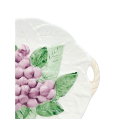 Een rond, wit keramisch bord met handvatten, versierd met een reliëf van paarse druiventrossen en groene bladeren.