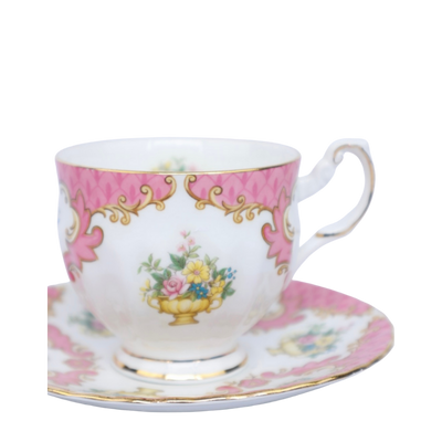 Een porseleinen theekopje met schoteltje, versierd met roze randen, gouden accenten en een bloemenboeket in het midden.